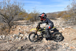 2025 Surron Hyper Bee electric dirt bike performing a mid-air jump on a rugged European off-road track.