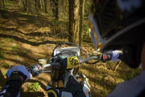 Sur Ron Storm Bee electric dirt bike in motion on a forest trail, rider leaning into a turn, dust kicking up. Dynamic off-road action shot.